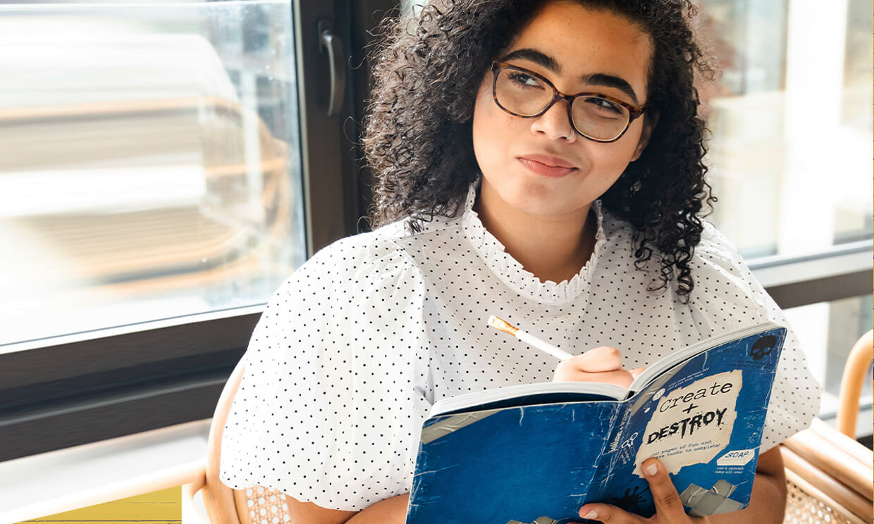 a woman holding a book pen and a book that says create and destroy.