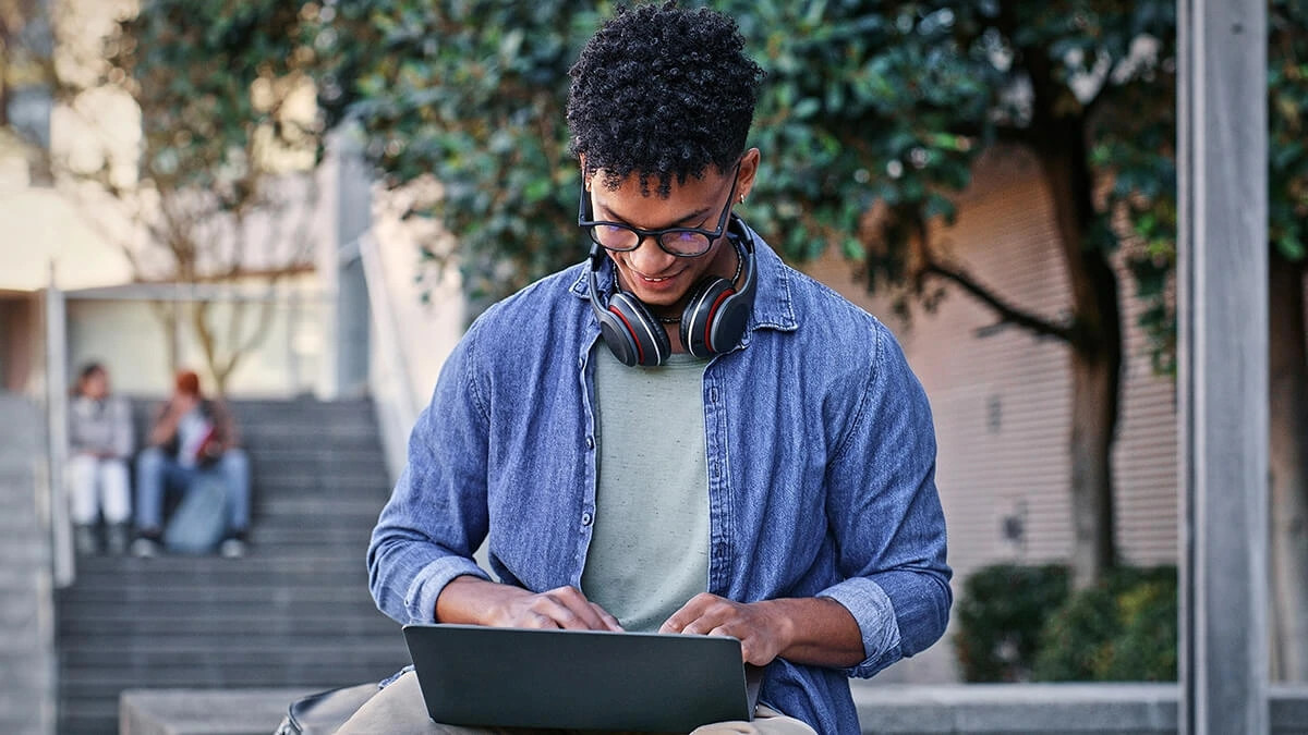 University student using a laptop outdoors on campus.